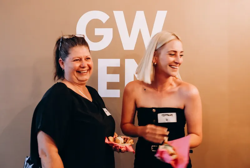 Two women laughing in front of the GWEN wall, The Foundation